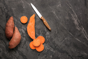 Knife with raw sweet potato on dark background
