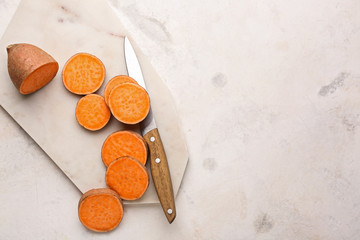 Cutting board and knife with raw sweet potato on light background