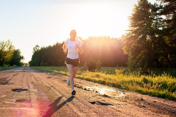  Athlete runner feet running on the dirt road across the field in the sunrise.