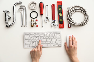 Plumbing tools and woman with computer keyboard on white background, top view