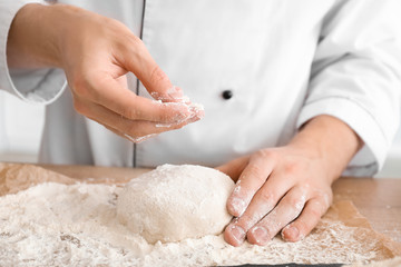 Man sprinkling dough with flour on table, closeup