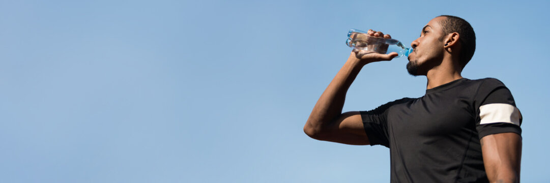 Afro Man Drinking Water After Running On Blue Sky Background