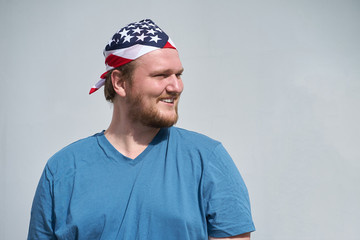 Portrait of young caucasian smiling man with USA flag bandana covered obove his head