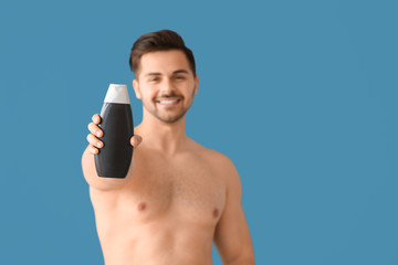 Handsome man with bottle of shampoo on color background