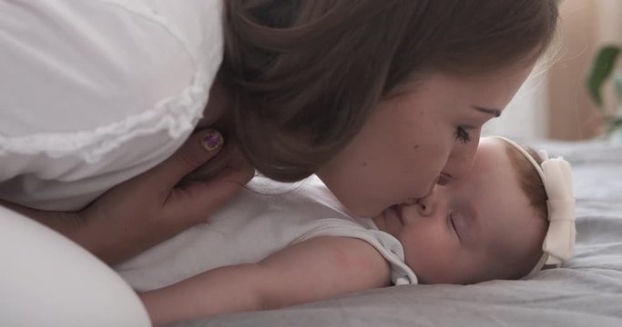 Happy mother kissing her cute baby daughter on bed