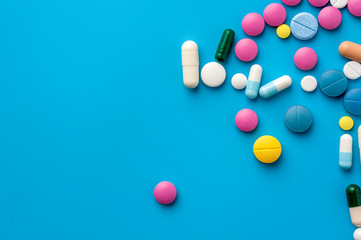 Flat lay - multicolored pills, drugs and capsules on blue background