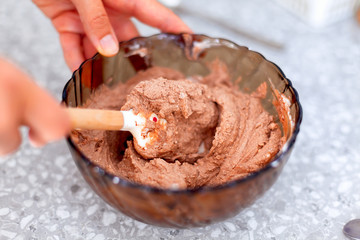 Woman hands with spatula mixes chocolate cream in bowl.