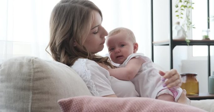 Young mother consoling her cute baby daughter on sofa in the living room
