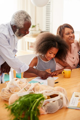 Grandparents Sitting At Table Helping Granddaughter With Homework