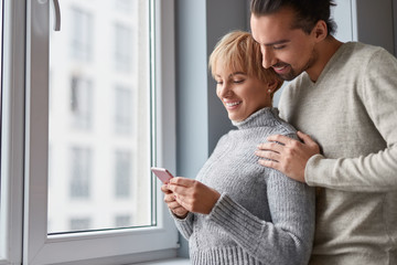 Fototapeta premium Couple using smartphone near window