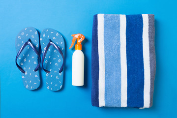 Top view of Beach flat lay accessories. sunscreen bottle with towel and flip-flop on Bluebackground with copy space