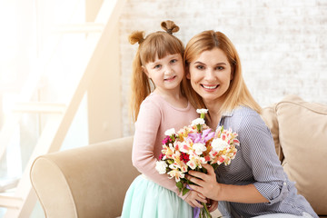 Fototapeta na wymiar Little girl greeting her mother with bouquet of flowers at home