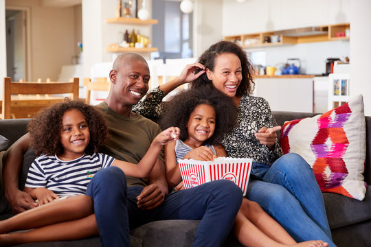 Family Sitting On Sofa At Home Eating Popcorn And Watching Movie Together