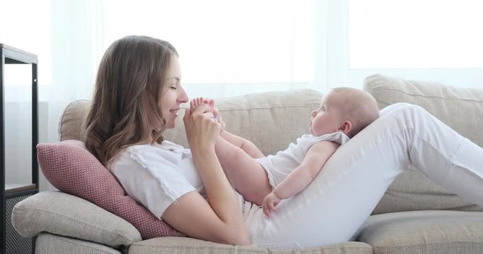 Relaxed mother playing with her cute baby daughter on sofa at home