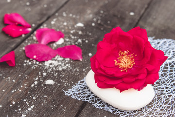 Natural cosmetic soap with red rose and petals on a dark wooden background.
