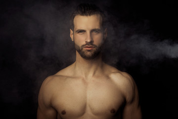 Handsome sport sexy stripped guy portrait in a water draps and fog smoke mist on isolated black background