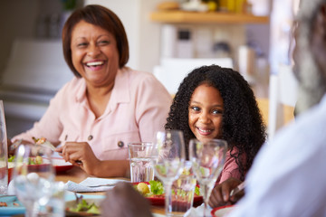 Multi-Generation Family Sitting Around Table At Home Enjoying Meal Together