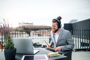 A young businessman with headphones sitting on a terrace, having fun.
