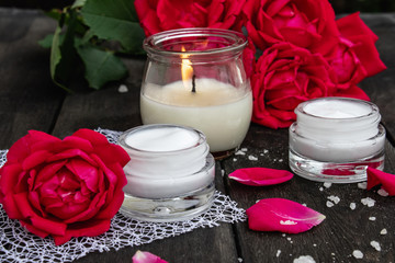 cosmetic cream and roses with petals and a burning candle on the old wooden background.