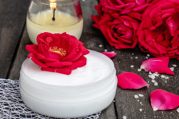 cosmetic cream and roses with petals and a burning candle on the old wooden background.