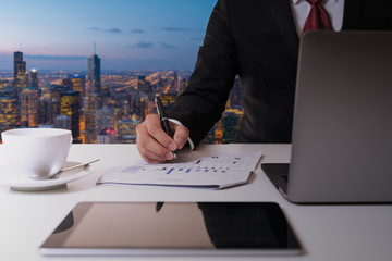 Hand's businessman holding pen and analysis data chart on document paper and looking computer at...