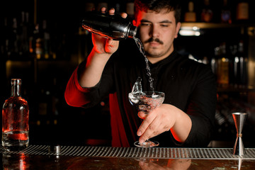 Professional bartender pouring a transparent alcohol into the glass from the steel shaker