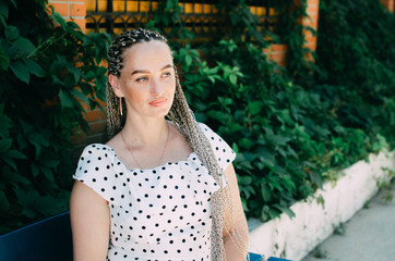 Beautiful girl with braided pigtails on the bench, on the background of a climbing plant