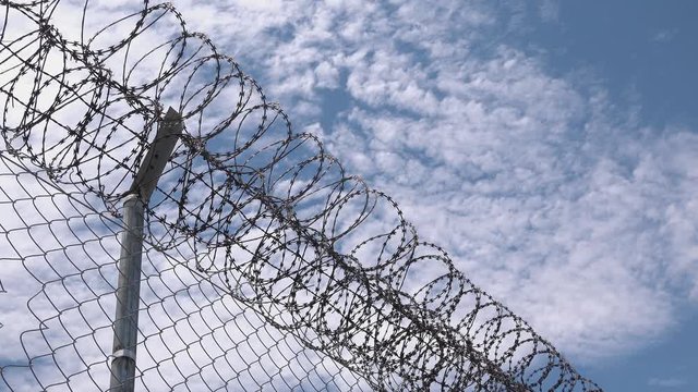 Medium Shot of a Barbed Wire Fence with Fluffy Clouds in the Background