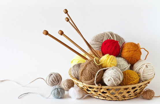 Сolorful balls of wool yarn and knitting wooden needles in a wicker basket on a white background. Still life, place for text, closeup