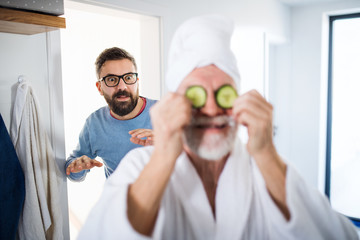 An adult hipster son and senior father in bathroom indoors at home, having fun.