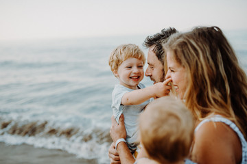 A young family with two toddler children standing on beach on summer holiday.