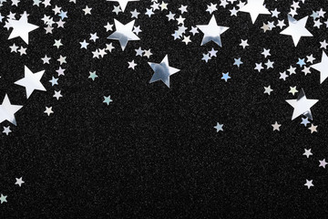 Falling silver stars confetti on black Festive holiday background. Glowing sparkles frame, flat lay, copy space.
