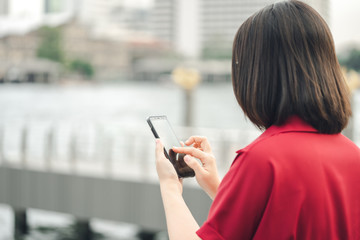 A beautiful Asian woman uses a smartphone in the city center to search for various places. Restaurant reviews And send a message with copy space.