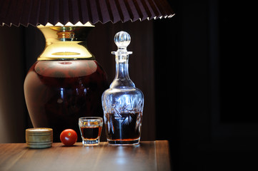 The decanter of whiskey, a stack of whiskey, a cherry tomato and a cup of salt under the lamp on...