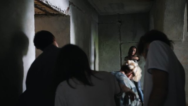 A zombie apocalypse. Survived woman with a gun walking out from the wall and aiming in the zombies