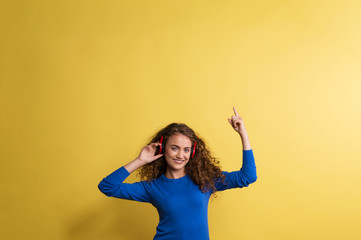 Portrait of a young woman with headphones in a studio on a yellow background.
