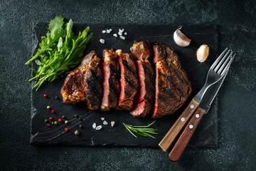  Sliced steak ribeye, grilled with pepper, garlic, salt and thyme served on a slate chopping Board on a dark stone background. Top view. Flat lay © Vasiliy