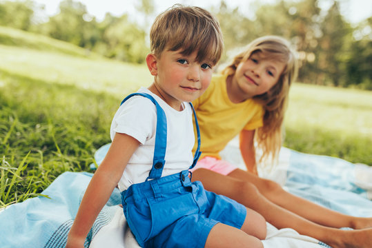 Outdoors image of happy children playing on the blanket outdoors. Little boy and cute little girl relaxing in the park. Adorable kids having fun on sunlight. Sister and brother spending time together.