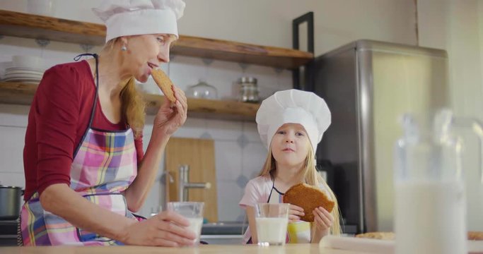 Side view of grandmother and granddaughter bite big homemade cookies and enjoy taste