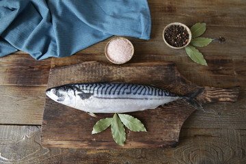 Fresh mackerel with salt, pepper and bay leaves on a wooden cutting board and wooden rustic background with copy space for text. Flat lay. Top view. 
