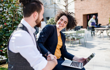Young businesspeople with laptop outdoors in courtyard, expressing excitement.