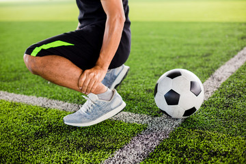 Soccer ball on green artificial turf with footballer is sitting and catch the ankle