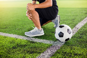 Soccer ball on green artificial turf with footballer is sitting and catch the knee.