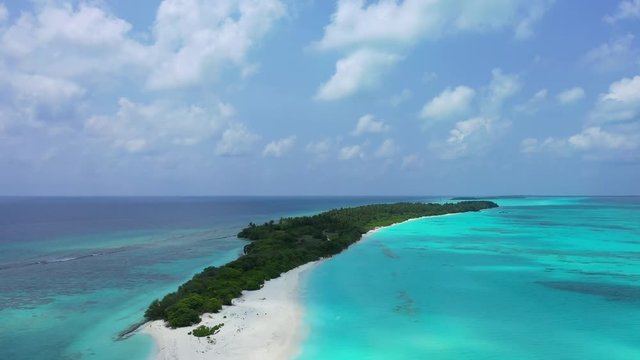 Drone rising in the sky while filming a very long sandy island near the coral reef in the Maldives islands, Indian Ocean. Pure turquoise waters all around of it