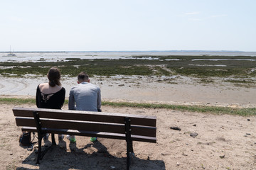 young couple sitting on beach bench in summer sea background low tide