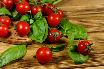 Fresh cherry tomatoes with green basil leaves on a wooden table