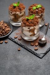 Classic tiramisu dessert in a glass on stone serving board on dark concrete background