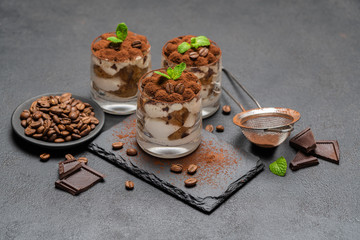 Classic tiramisu dessert in a glass on stone serving board on dark concrete background