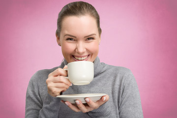 young woman enjoys a cup off coffee or tea in front of a pink background