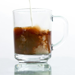 milk poured into a transparent cup of black coffee